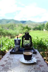 Coffee cup on table against sky on field