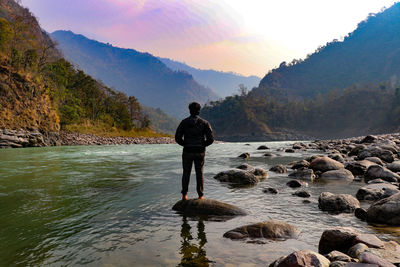 Rear view of man standing on rock against sky