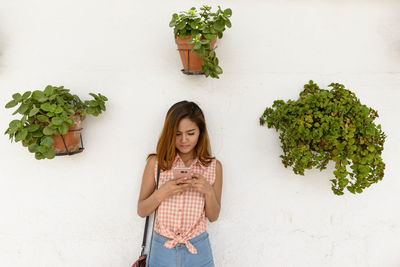 Young woman drinking drink against wall