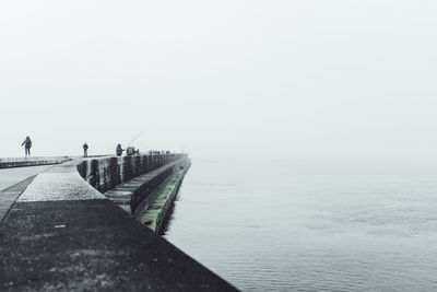 People fishing on pier over sea against clear sky