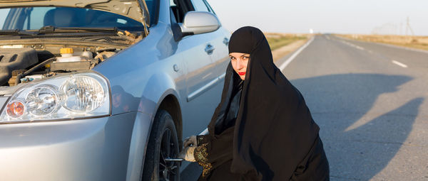 Portrait of woman in burka replacing tire on road