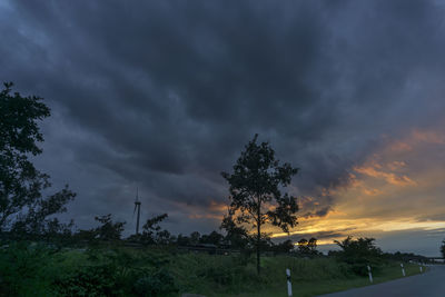 Trees on field against dramatic sky