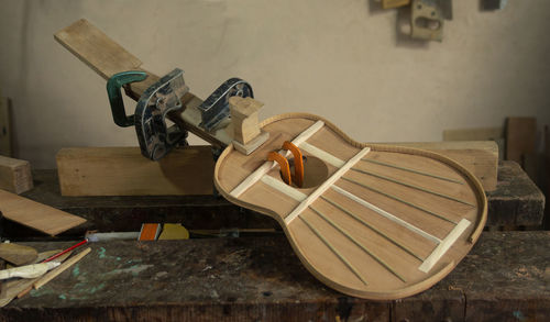 Wooden guitar in assembly process with presses holding parts on carpenter's workbench