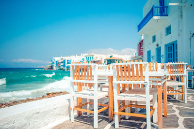 Chairs and tables on beach by sea against blue sky