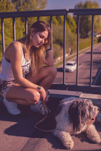 Smiling young woman crouching by dog on footbridge