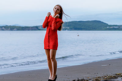 Young woman standing at beach against sky