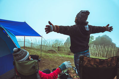 Man with arms outstretched standing by woman at campsite