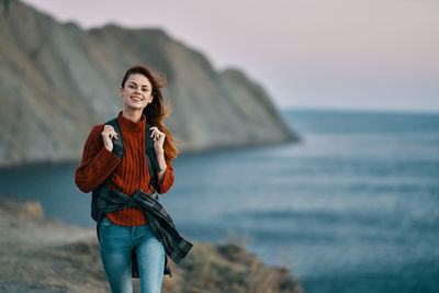 Portrait of smiling young woman standing in sea against sky