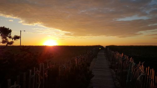 Footpath amidst field against sky during sunset