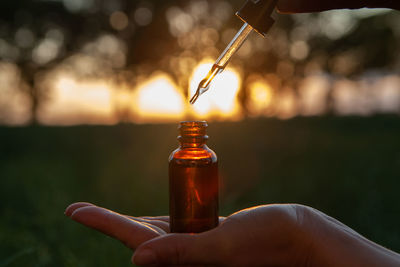 Close-up of hand holding glass bottle during sunset