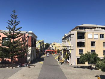 Empty road amidst buildings against clear blue sky