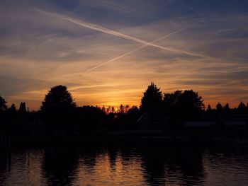 Silhouette trees by river against sky at sunset