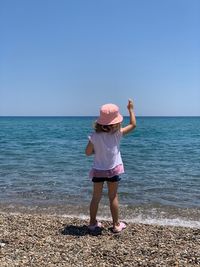 Rear view of girl wearing hat standing on beach against sky