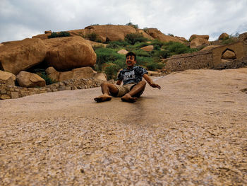 Man sitting on rock against sky