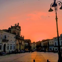 Street by buildings against sky at sunset