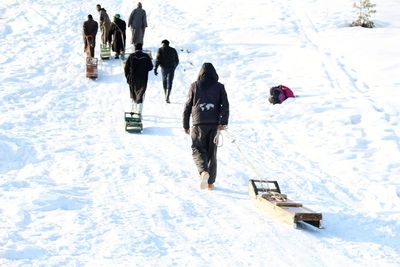 Rear view of people with sled walking on snowcapped mountain during winter