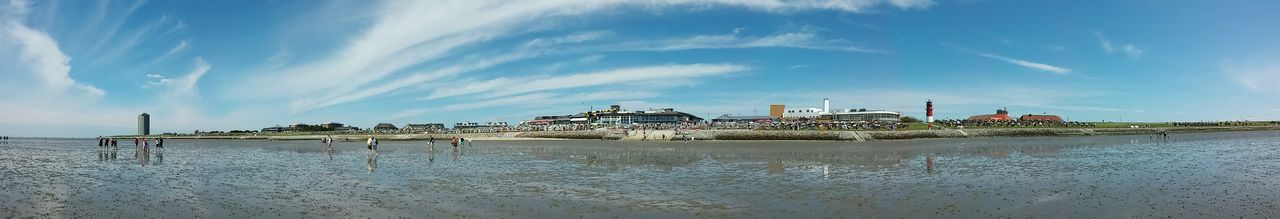 sky, water, sea, beach, built structure, cloud - sky, architecture, shore, sand, horizon over water, cloud, blue, building exterior, incidental people, day, sunlight, nature, tranquility, large group of people, outdoors