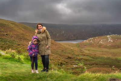 Mother and daughter standing and looking at camera, lough bray in background. wicklow mountains