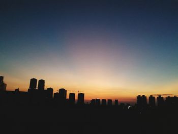 Silhouette cityscape against clear sky during sunset