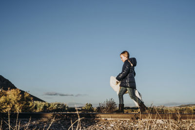 Kid hiking in the woods caring a sleeping bag walking in a train track