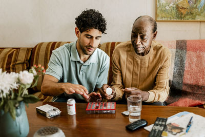 Male nurse explaining medicine dosage to senior man sitting on sofa at home