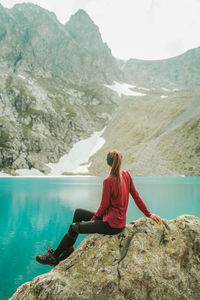 Full length of man sitting on rock by lake