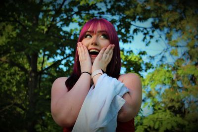 Young woman looking away while standing against trees