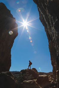 Low angle view of man standing amidst rock formations on sunny day