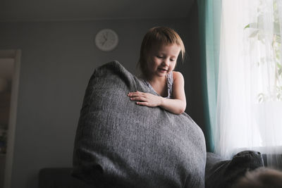 Kid toddler builds house from pillows on sofa in living room, lifestyle and games in real interior