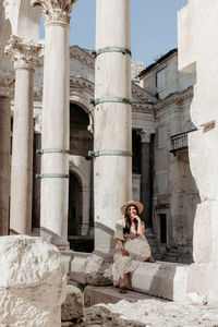 Young woman in beautiful dress sitting on wall of diocletian's palace in split, croatia.