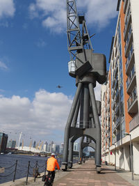 Low angle view of crane by building against sky