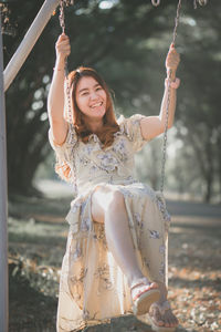 Portrait of smiling young woman on swing at land