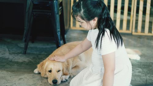 Side view of girl petting retriever dog while kneeling on floor