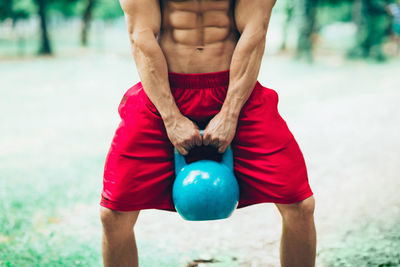 Midsection of shirtless man lifting kettlebell on field