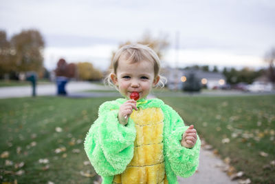 Happy toddler looking straight ahead eating red sucker on halloween