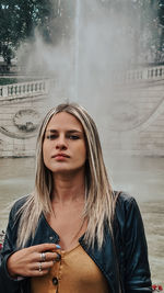 Portrait of young woman standing against waterfall