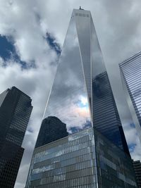 Low angle view of one world trade center and towers against cloudy sky