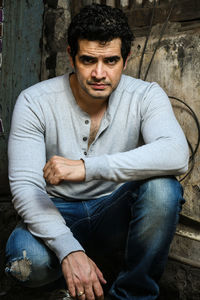 Portrait of young man crouching against building