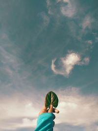 Low angle view of person holding a leaf against sky