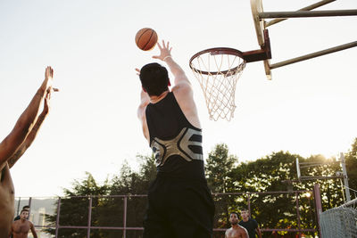 Man playing basketball with friends in court against clear sky