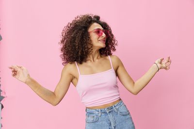 Portrait of young woman with arms raised against pink background