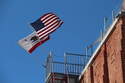 Low angle view of flags on railing against clear blue sky