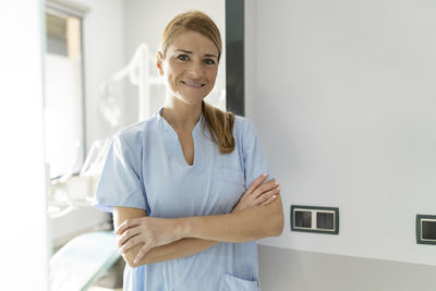 Smiling dentist standing with arms crossed in dental clinic