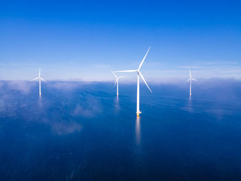 Wind turbines in sea against blue sky