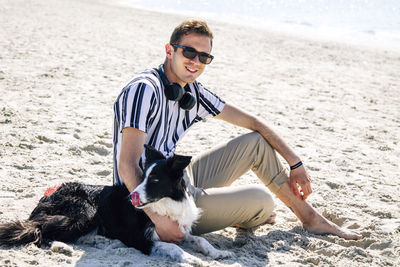 Portrait of young man with dog on sand at beach