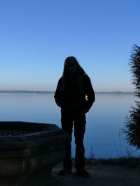 Man standing against lake against clear blue sky