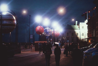 Rear view of people walking on illuminated street at night