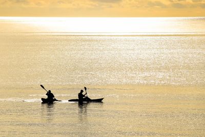 Silhouette people on sea against sky during sunset