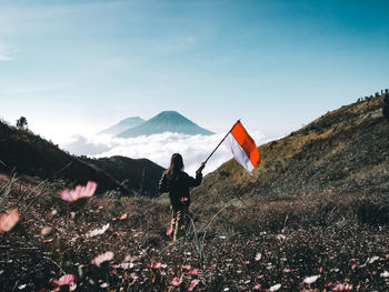 Woman standing with flag on field against mountains