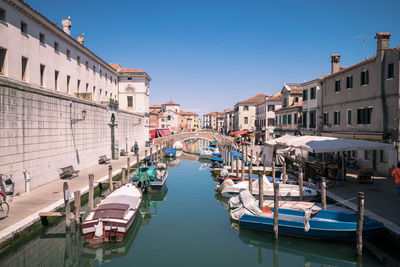 Boats moored in canal amidst buildings against clear blue sky